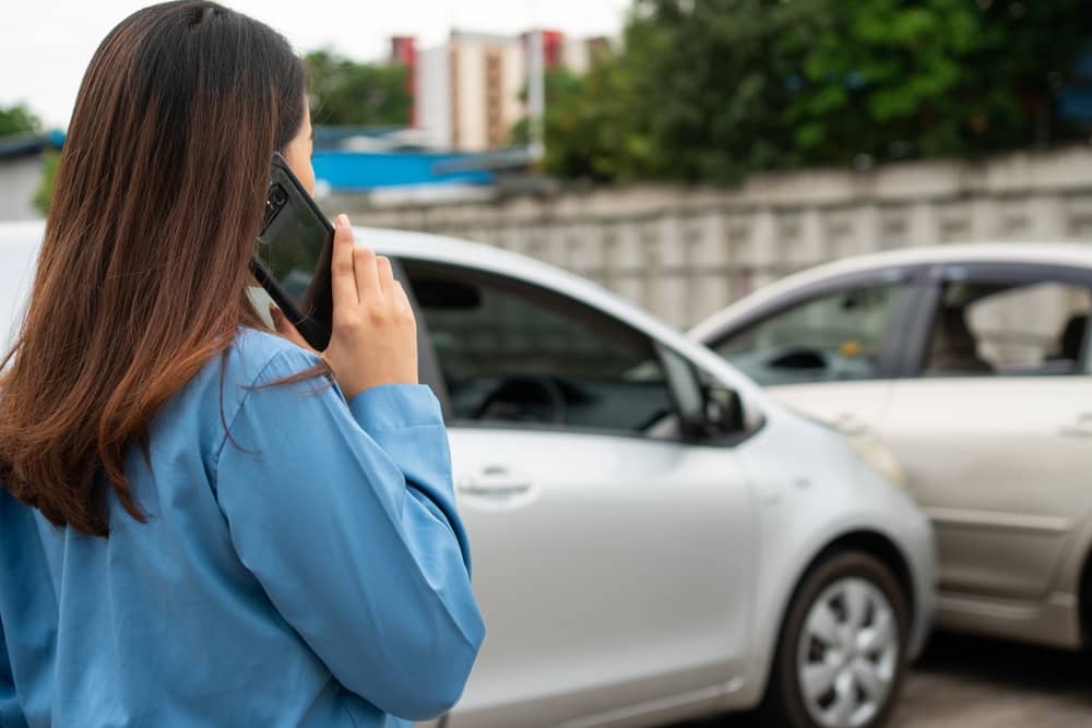 Photo of a girl with phone in hand standing in front of two cars